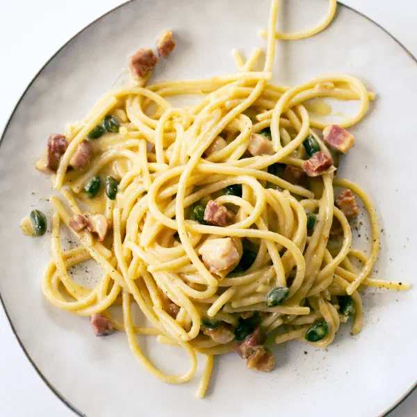 Spaghetti Carbonara mit Pistazien und Guanciale auf einem weißen Teller